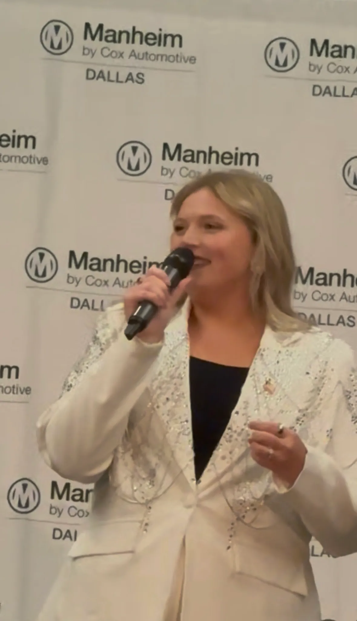 Grace Lakey speaking into a microphone on stage at a Manheim Dallas event