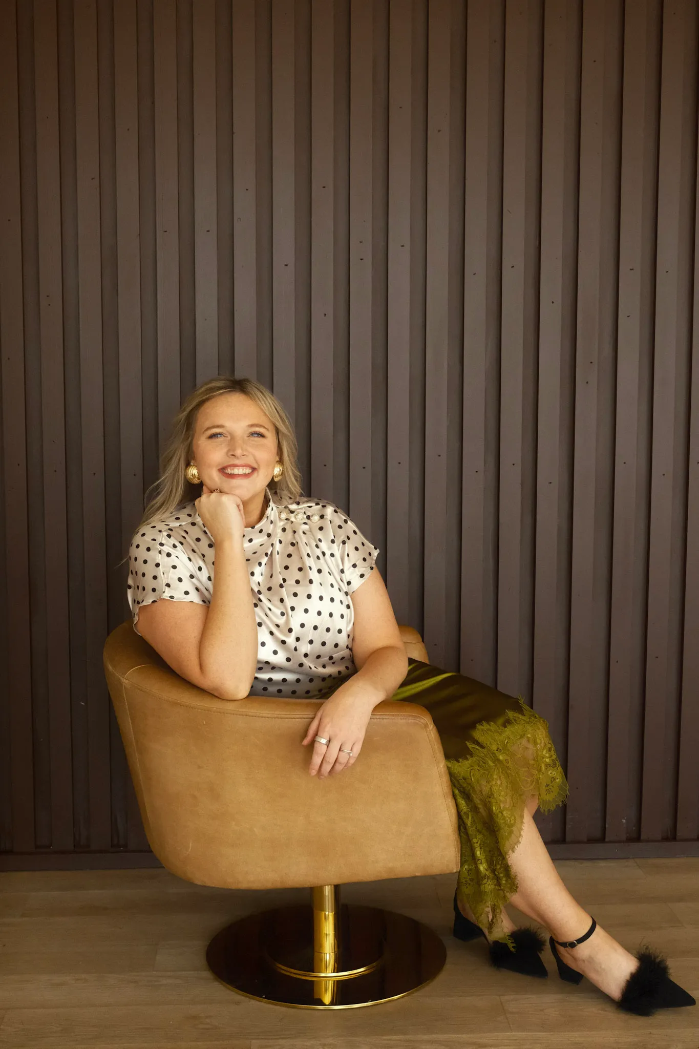 Grace Lakey sitting in a tan chair wearing a polka-dot top and olive skirt